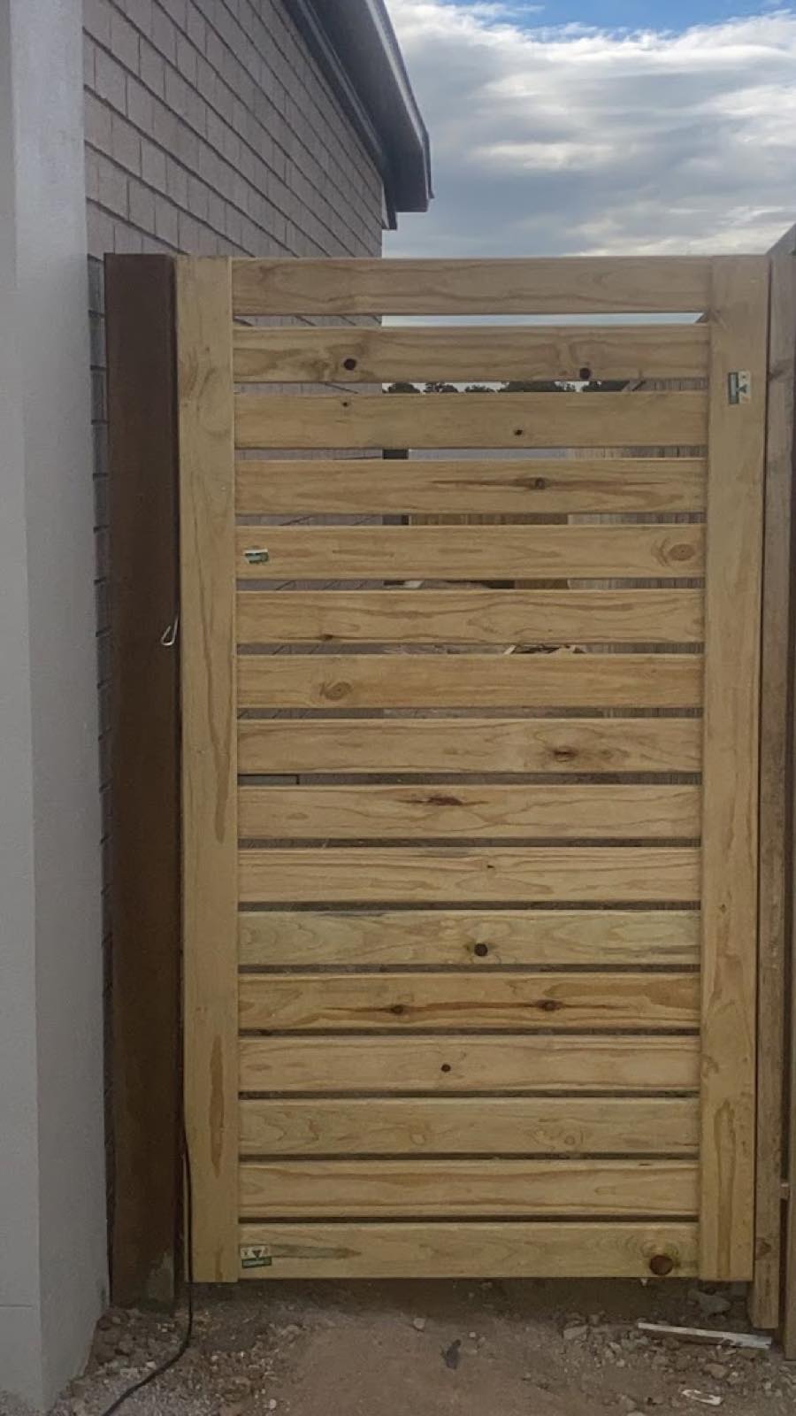 Horizontal-slat timber gate between a house wall and boundary fence