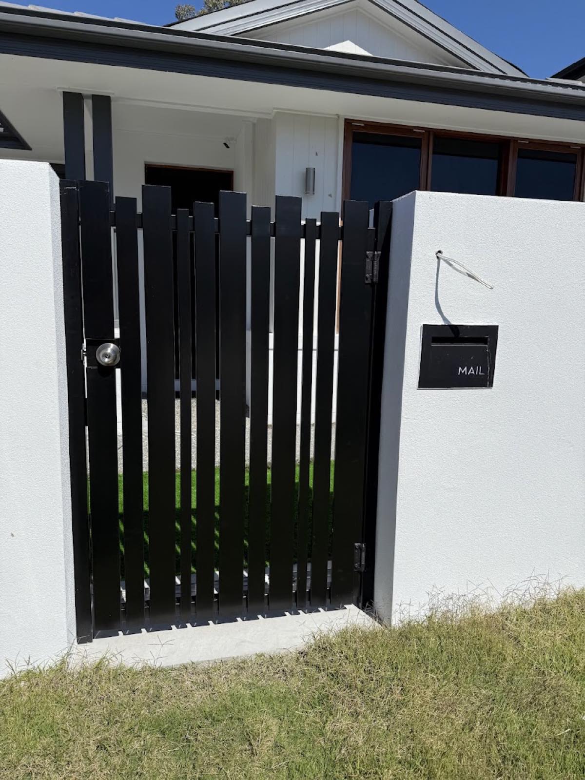 Black aluminium slat pedestrian gate beside a rendered pier